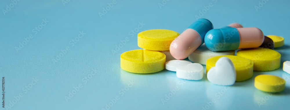 A pile of medical pills of different colors on a blue background. A pile of medical pills of different colors on a blue background.