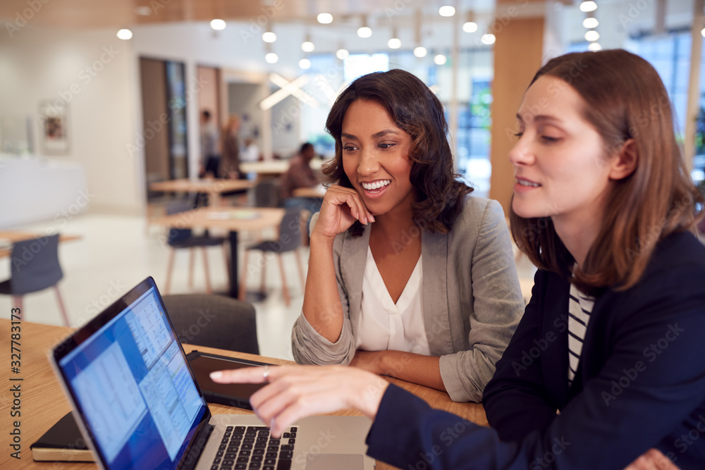 Two Businesswomen With Laptop At Desk In Open Plan Office Collaborating On Project Together Two Businesswomen With Laptop At Desk In Open Plan Office Collaborating On Project Together