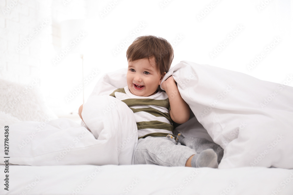 Cute little child playing under blanket in bed