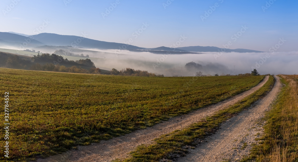 Povazsky Inovec Hill in Slovakia in the valley on sunrise. Landscape photo of field with green grass, fog and beautiful sun rays. Perfect view point from meadow on sunrise. Slovakia landscape.