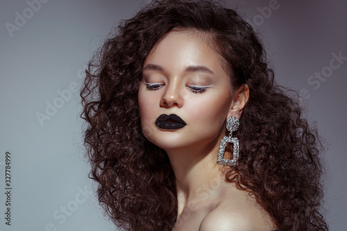 Beauty portrait of a beautiful girl with black lipstick on her lips and with lush curls on a gray background.