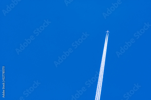Airplane with white condensation tracks. Jet plane on blue sky and white clouds with vapor trail. Travel by airplane concept. Trails of exhaust gas from airplane engine. Aircraft with white stripes.