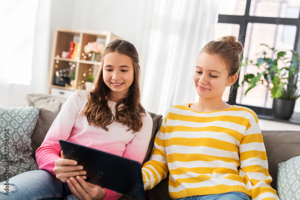 Obraz premium people, technology and friendship concept - happy teenage girls with tablet pc computer sitting on sofa at home