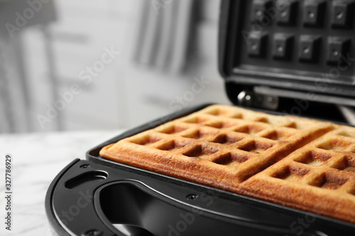 Modern iron with tasty Belgian waffles on table, closeup