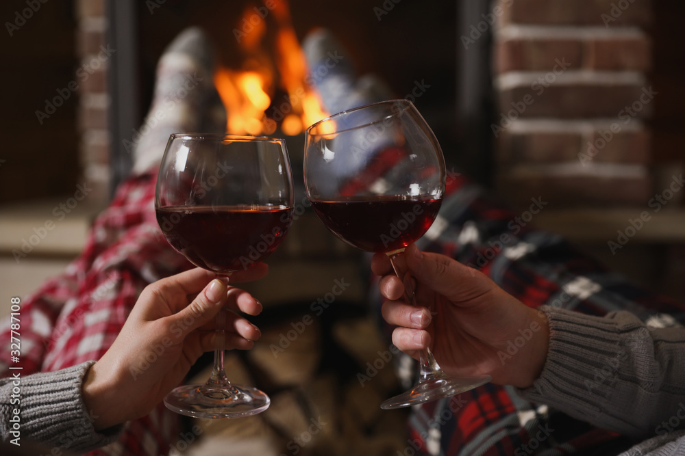 Couple with glasses of red wine near burning fireplace, closeup - obrazy, fototapety, plakaty 