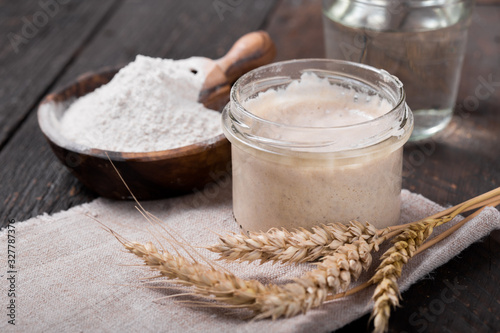 Fresh homemade bubbly sourdough starter, a fermented mixture of water and flour to use as leaven for bread baking, on wooden table