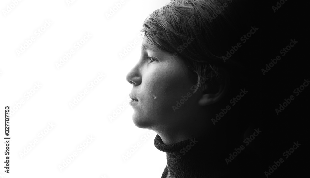 Black and white portrait of young sad boy crying with sad eyes. White background. Free space for text. Tear on cheek of unhappy teenager.