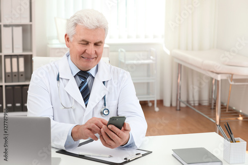 Senior doctor with smartphone at table in office