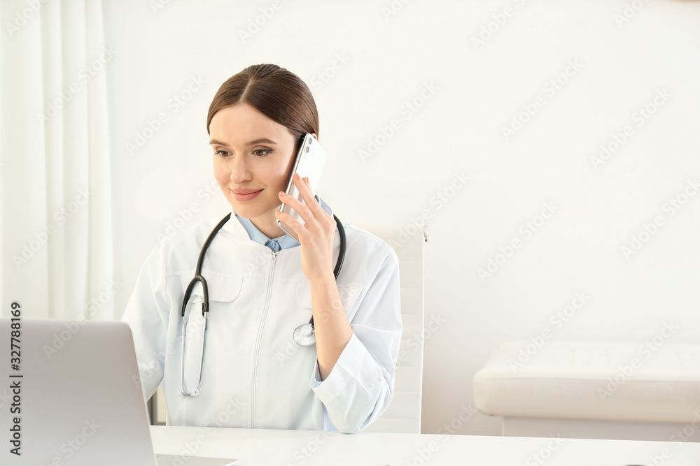 Young female doctor talking on phone at table in office Young female doctor talking on phone at table in office