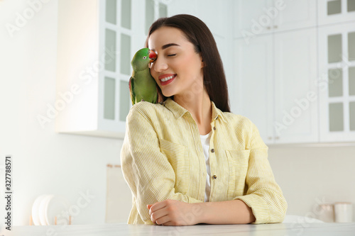 Foto Young woman with Alexandrine parakeet indoors. Cute pet