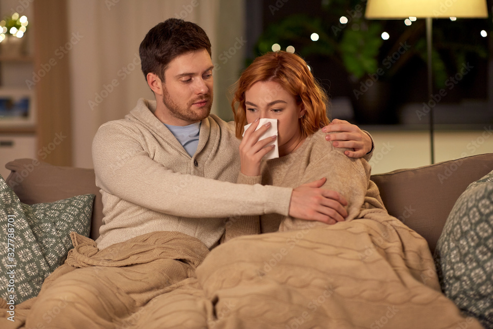 health, flu and people concept - sick young couple with tissue blowing nose at home health, flu and people concept - sick young couple with tissue blowing nose at home