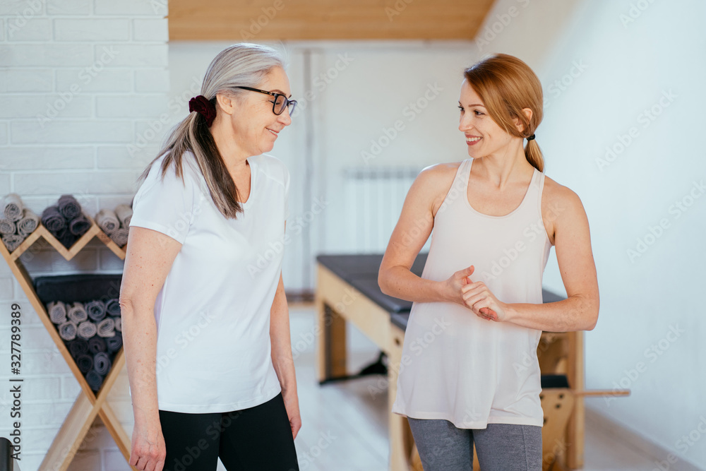 Obraz premium Positive friendly smiling female pilates instructor meeting mature elderly woman in pilates studio.