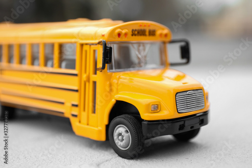 Yellow toy school bus against blurred background, closeup. Transport for students