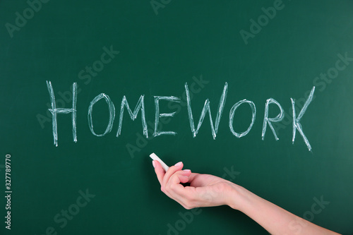 Woman writing word HOMEWORK on chalkboard, closeup