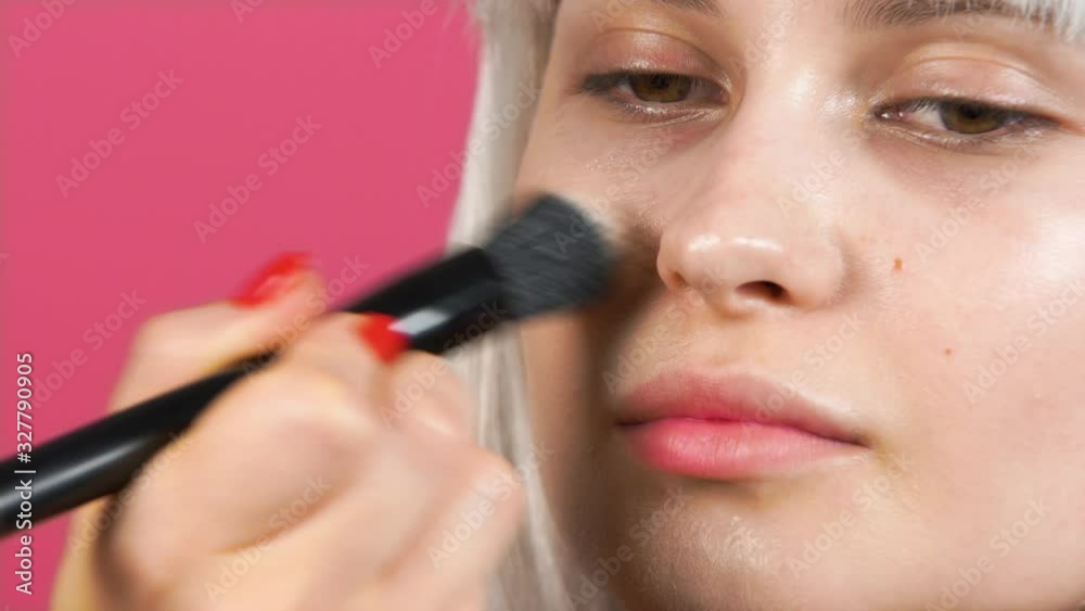 professional makeup. Close-up of a blonde model during makeup. the makeup artist brushes the foundation. young girl in a bob wig. studio shooting on a pink background. beauty salon concept professional makeup. Close-up of a blonde model during makeup. the makeup artist brushes the foundation. young girl in a bob wig. studio shooting on a pink background. beauty salon concept
