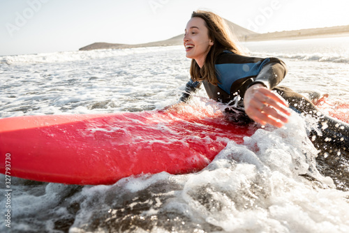 Konstfotografi Young woman in wetsuit catching water flow on the surfboard, surfing on the wavy ocean during a sunset
