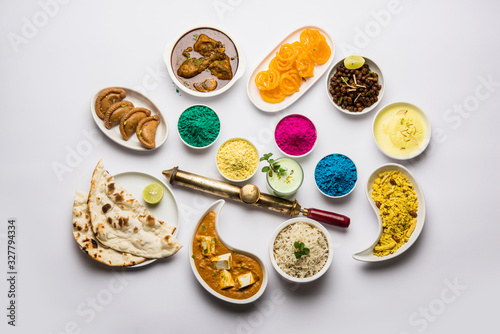 Happy Holy concept  showing Indian assorted lunch food like paneer butter masala  naan  jeera rice  black chana fry  jalebi  fujiyama  thandai and Farsan with holi colours and pichkari 