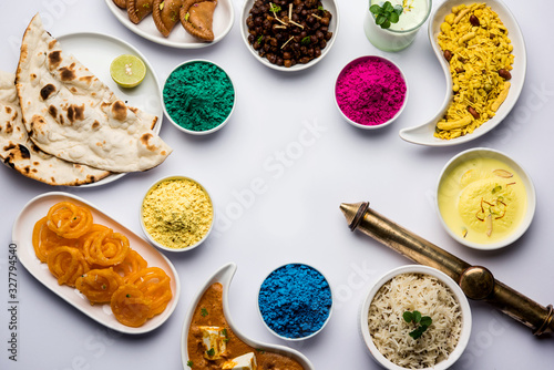 Happy Holy concept  showing Indian assorted lunch food like paneer butter masala, naan, jeera rice, black chana fry, jalebi, fujiyama, thandai and Farsan with holi colours and pichkari 