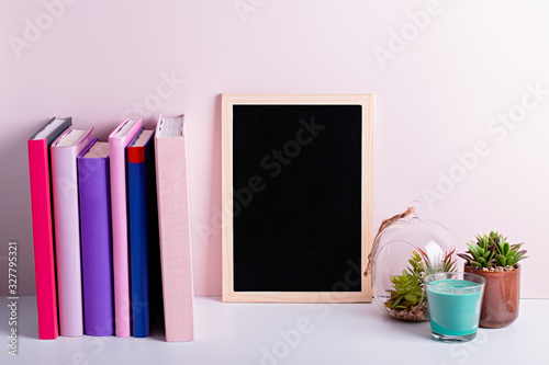 Bookshelf with multicolor books, house plants succulents and black board frame for text. Background for Teacher's Day, World Book Day. Still life with stack of colorful books and chalkboard