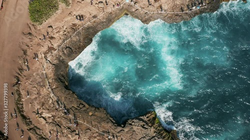4k overhead aerial view of people watching rough, breaking ocean waves and a natural blowhole on a rocky coastline