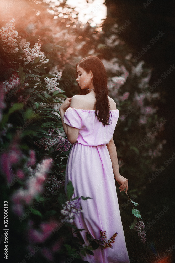 Beautiful young girl in a pink dress posing in flowers. Posing and enjoying the spring. Art work of romantic woman .Pretty tenderness model looking at camera.