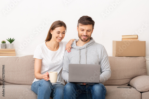 Smiling young couple with laptop planning repair in their new house