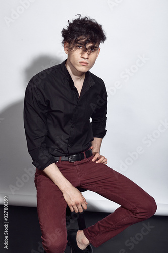 Young guy in a black shirt similar to Adriano Celentano posing on a white background. Fashion portrait photo