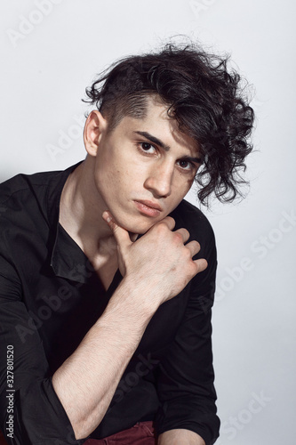 Young guy in a black shirt similar to Adriano Celentano posing on a white background. Fashion portrait photo