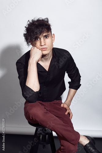Young guy in a black shirt similar to Adriano Celentano posing on a white background. Fashion portrait photo