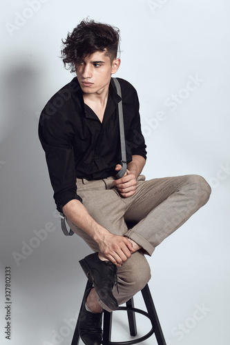 Young guy in a black shirt similar to Adriano Celentano posing on a white background. Fashion portrait photo