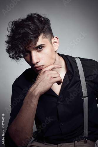 Young guy in a black shirt similar to Adriano Celentano posing on a white background. Fashion portrait photo