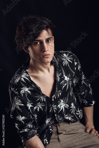 Young guy in a black shirt similar to Adriano Celentano posing on a black background. Fashion portrait photo