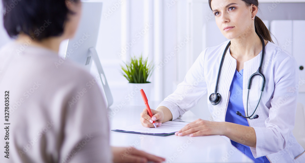 Doctor and patient discussing medical problems in a hospital consulting room. Doc filling in a patient's form Doctor and patient discussing medical problems in a hospital consulting room. Doc filling in a patient's form