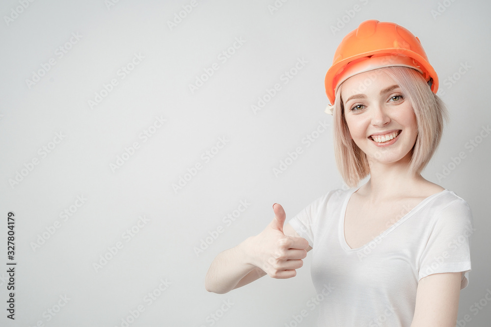 Portrait of a young girl in a white T-shirt and a construction helmet on a white background, showing thumbs up