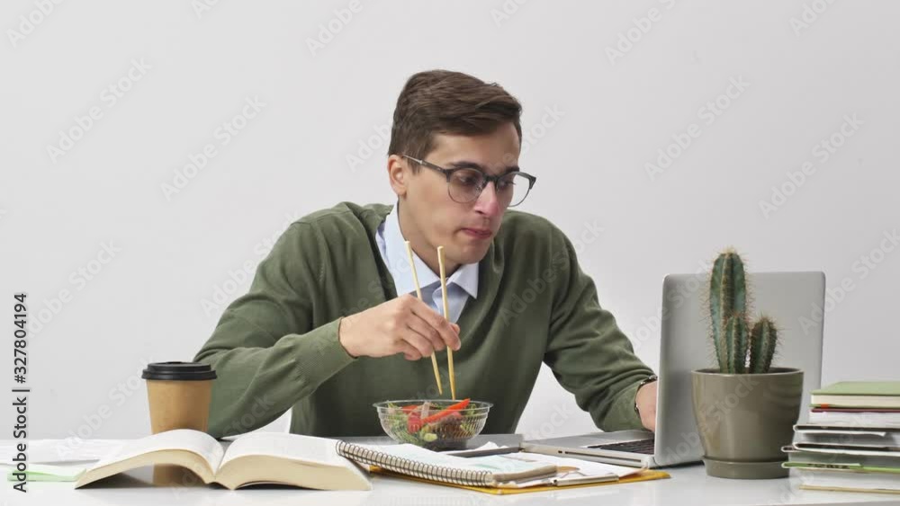 A focused young businessman is eating dinner at working time sitting at the table over white background A focused young businessman is eating dinner at working time sitting at the table over white background