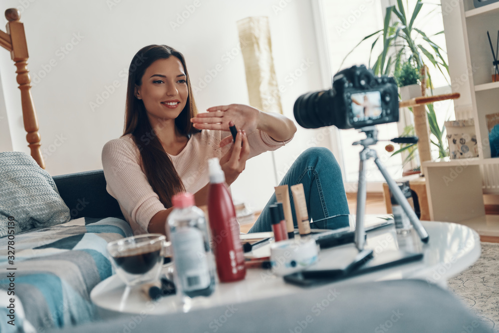 Beautiful young woman pointing at beauty product and smiling while making social media video Beautiful young woman pointing at beauty product and smiling while making social media video