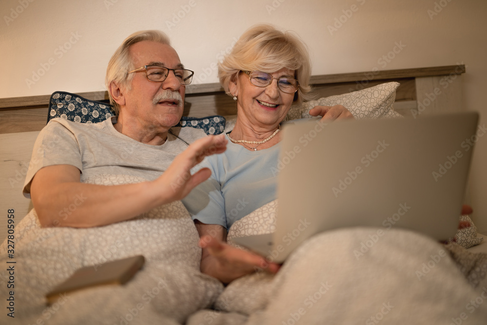 Happy mature couple having video call over laptop while lying down in bed. Happy mature couple having video call over laptop while lying down in bed.