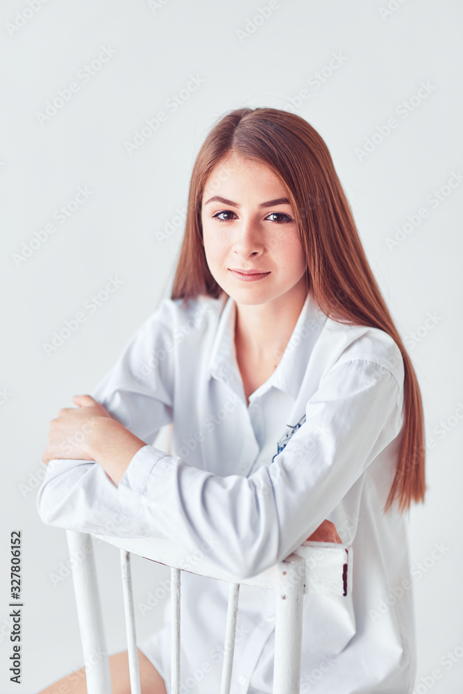 Pensive girl sitting on the white chair, white background. Pensive girl sitting on the white chair, white background.