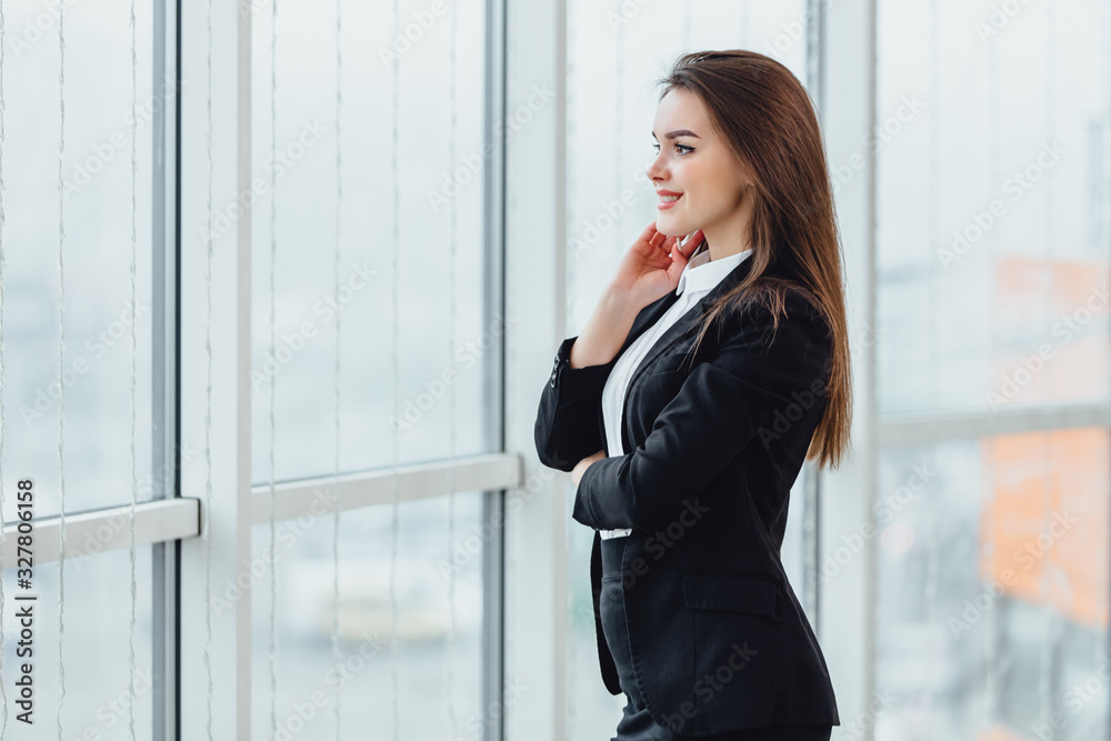 Cheerful female stands looking in the window, in her new office expressing pleasant emotions and confidence. Cheerful female stands looking in the window, in her new office expressing pleasant emotions and confidence.