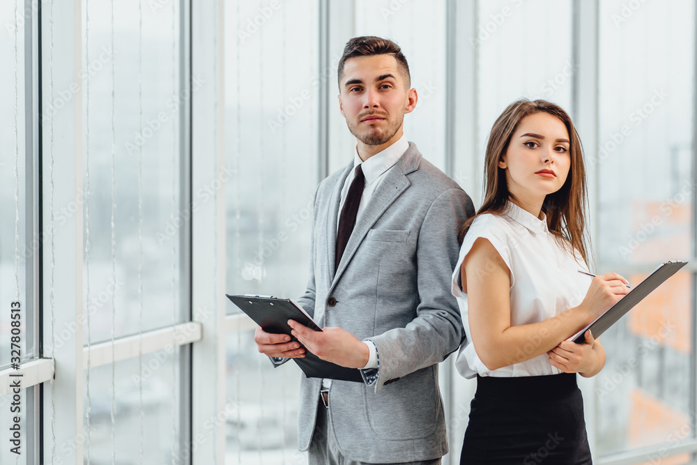 Happy business couple stabding side by side, holding clipboards, looking decisively at the camera. Happy business couple stabding side by side, holding clipboards, looking decisively at the camera.