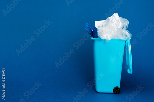 toy trash can with rubbish on blue background with copy space