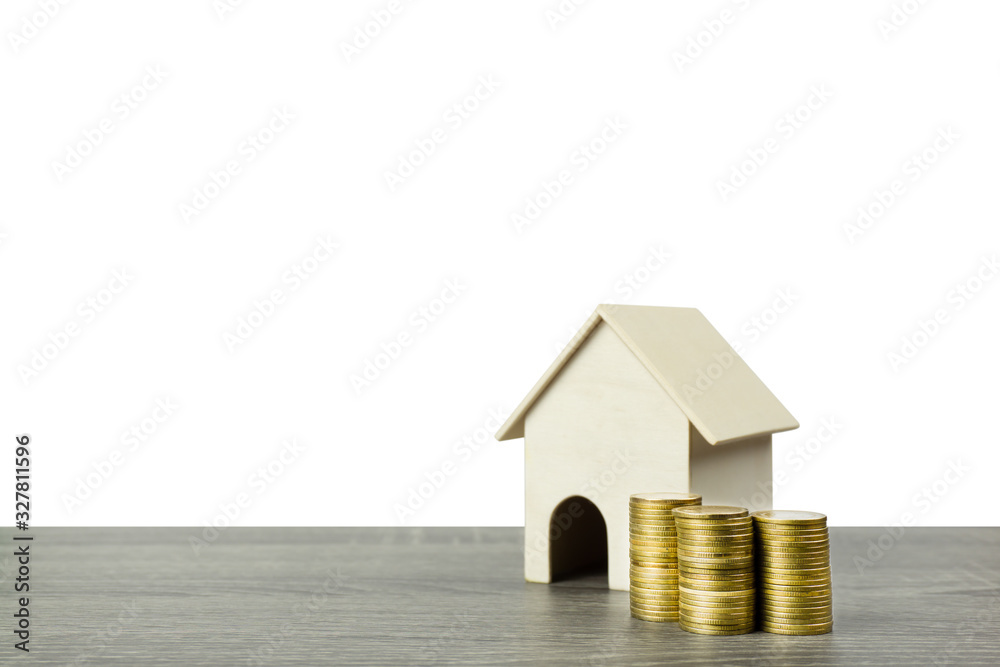 A small wooden house model with stack of golden coins on wood table isolated on white background. A small wooden house model with stack of golden coins on wood table isolated on white background.
