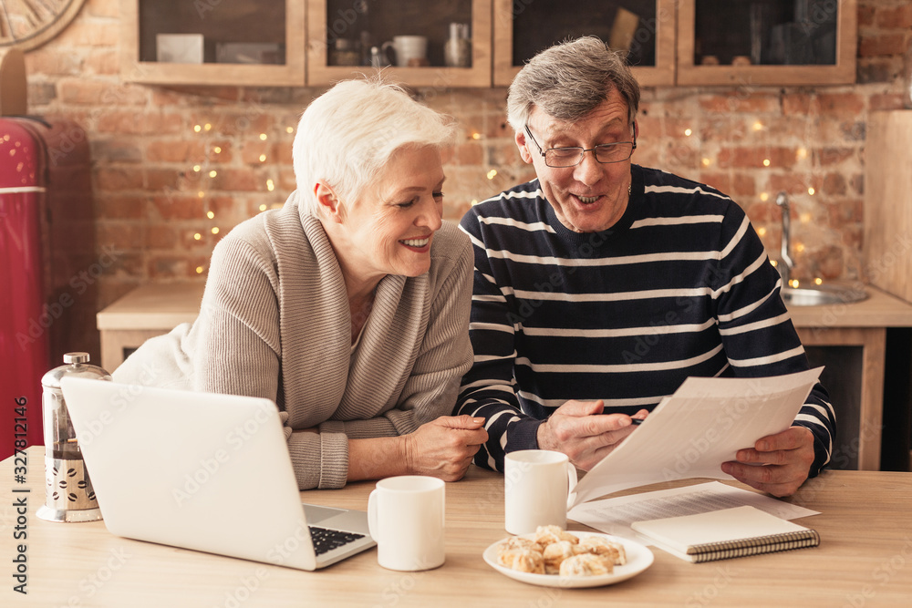 Smiling Senior Couple Reading Health Insurance Policy Contract In Kitchen Together - obrazy, fototapety, plakaty 