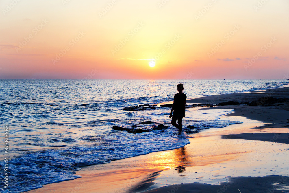 Silhouette of a young woman walking at the beach in front of the sunset Silhouette of a young woman walking at the beach in front of the sunset