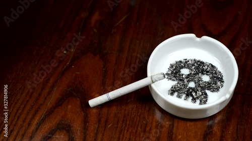Image skull from ash inside ashtray on brown table. Smoldering cigarette on ashtray. photo