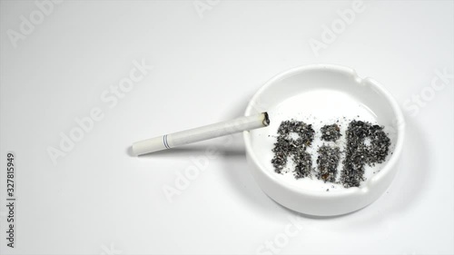 Image with word RIP transform into skull from ash inside ashtray on white. Smoldering cigarette on ashtray. photo