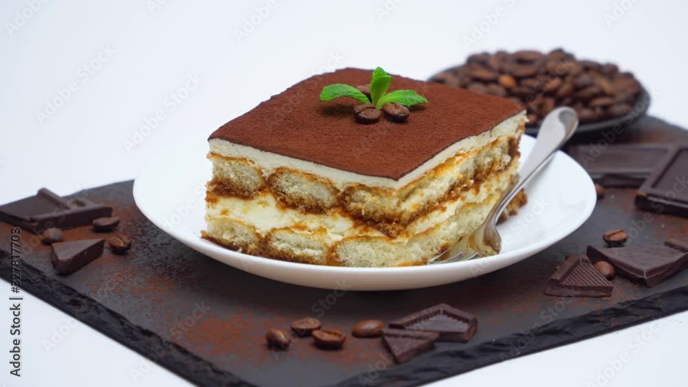 Tiramisu dessert portion, pieces of chocolate bar and coffee beans on stone serving cutting board Tiramisu dessert portion, pieces of chocolate bar and coffee beans on stone serving cutting board