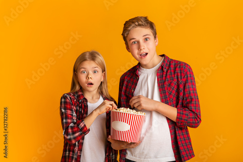 Shocked siblings eating popcorn and opening mouth in amazement
