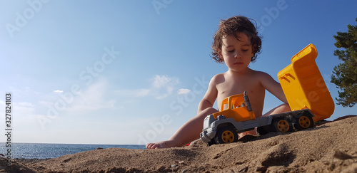 a little boy playing with toy truck on the beach on a hot summer day