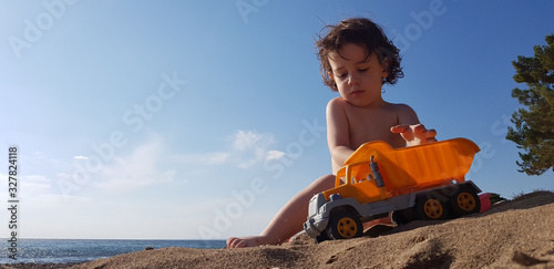 a little boy playing with toy truck on the beach on a hot summer day